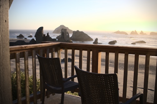 Sunlit holiday apartment balcony with comfortable chairs and panoramic coastal views.