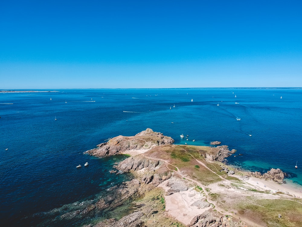 grama verde coberta montanha perto do mar azul sob o céu azul durante o dia