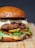 A gourmet hamburger with melted cheese, truffle slices, and a variety of toppings including pickles, arugula, and red bell pepper slices, all placed between a toasted bun. The presentation is on a wooden surface, showcasing a savory and tempting look.