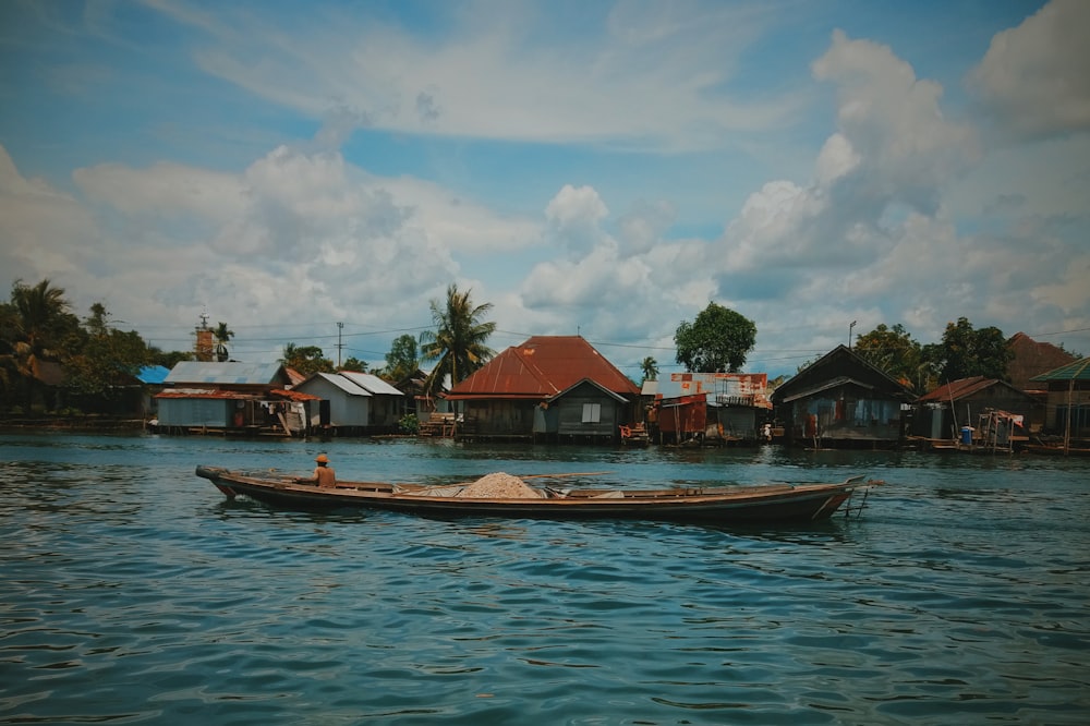 Barco marrón en cuerpo de agua cerca de casas bajo cielo nublado azul y blanco durante el día
