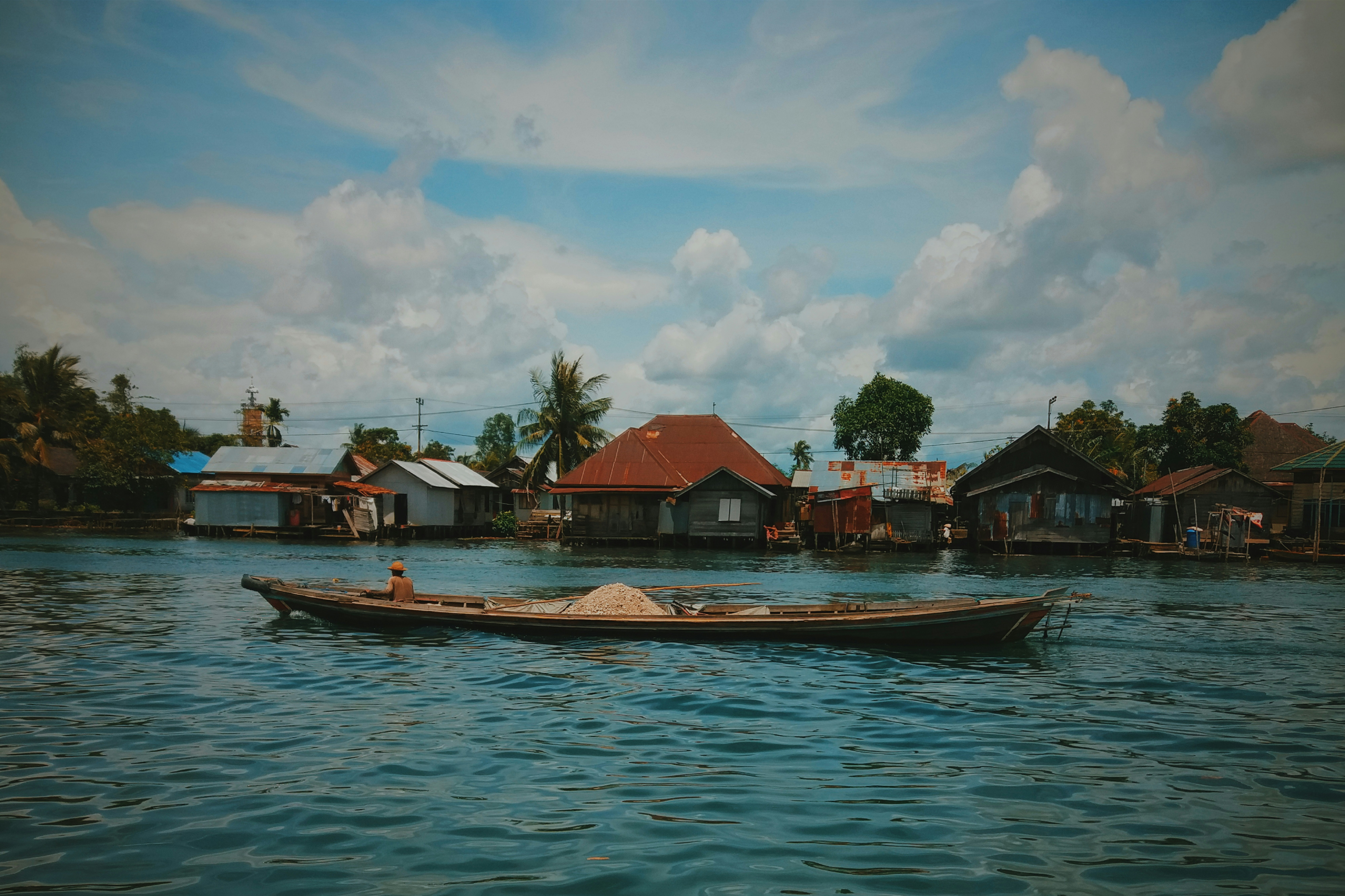 brown boat on body of water near houses under blue and white cloudy sky during daytime