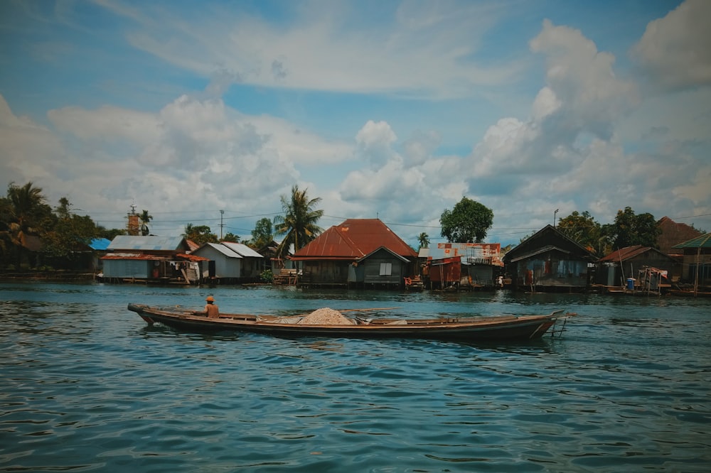 brown boat on body of water near houses under blue and white cloudy sky during daytime