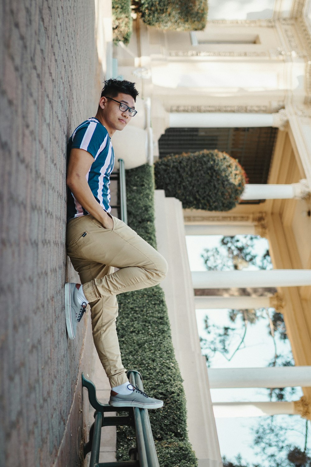 man in blue and white stripe polo shirt and brown pants sitting on brown wooden fence