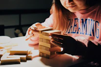 Close-up of a child’s hands carefully stacking wooden blocks on a soft rug.