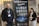 Two individuals stand on either side of a large banner for the BioPharmaceuticals Academy Masterclass. They both wear name tags and appear to be smiling. The banner lists various topics related to pharmaceuticals, including biologics and cell banks.