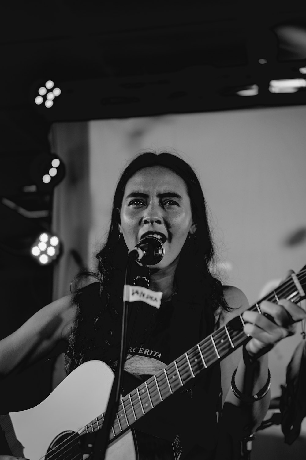 grayscale photo of woman singing and playing guitar