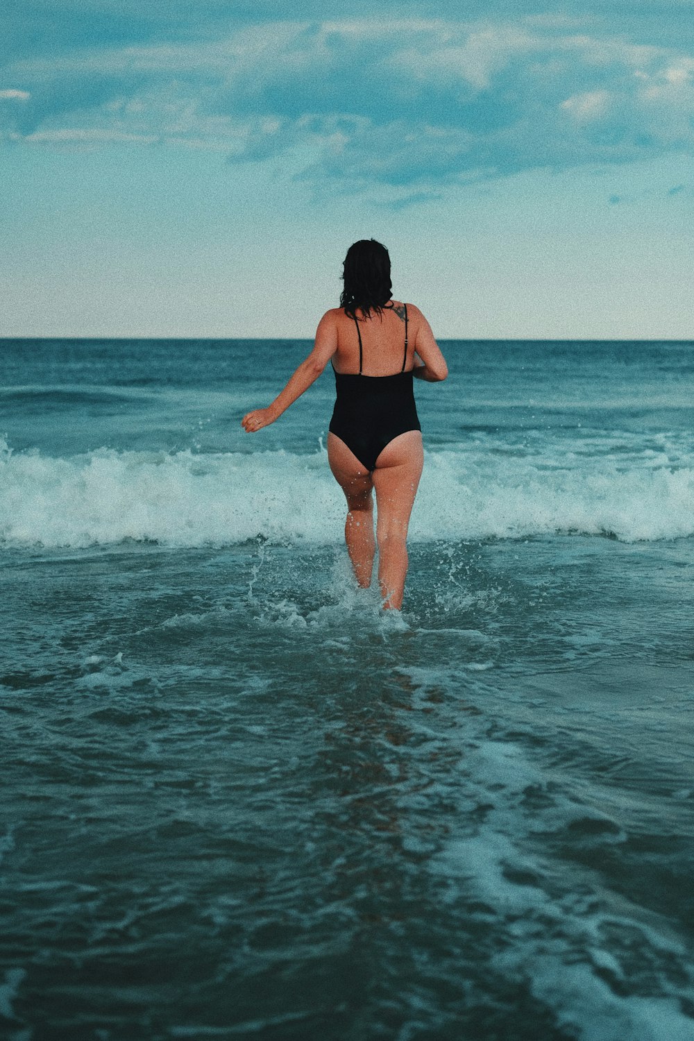 donna in costume da bagno nero in piedi sull'acqua di mare durante il giorno