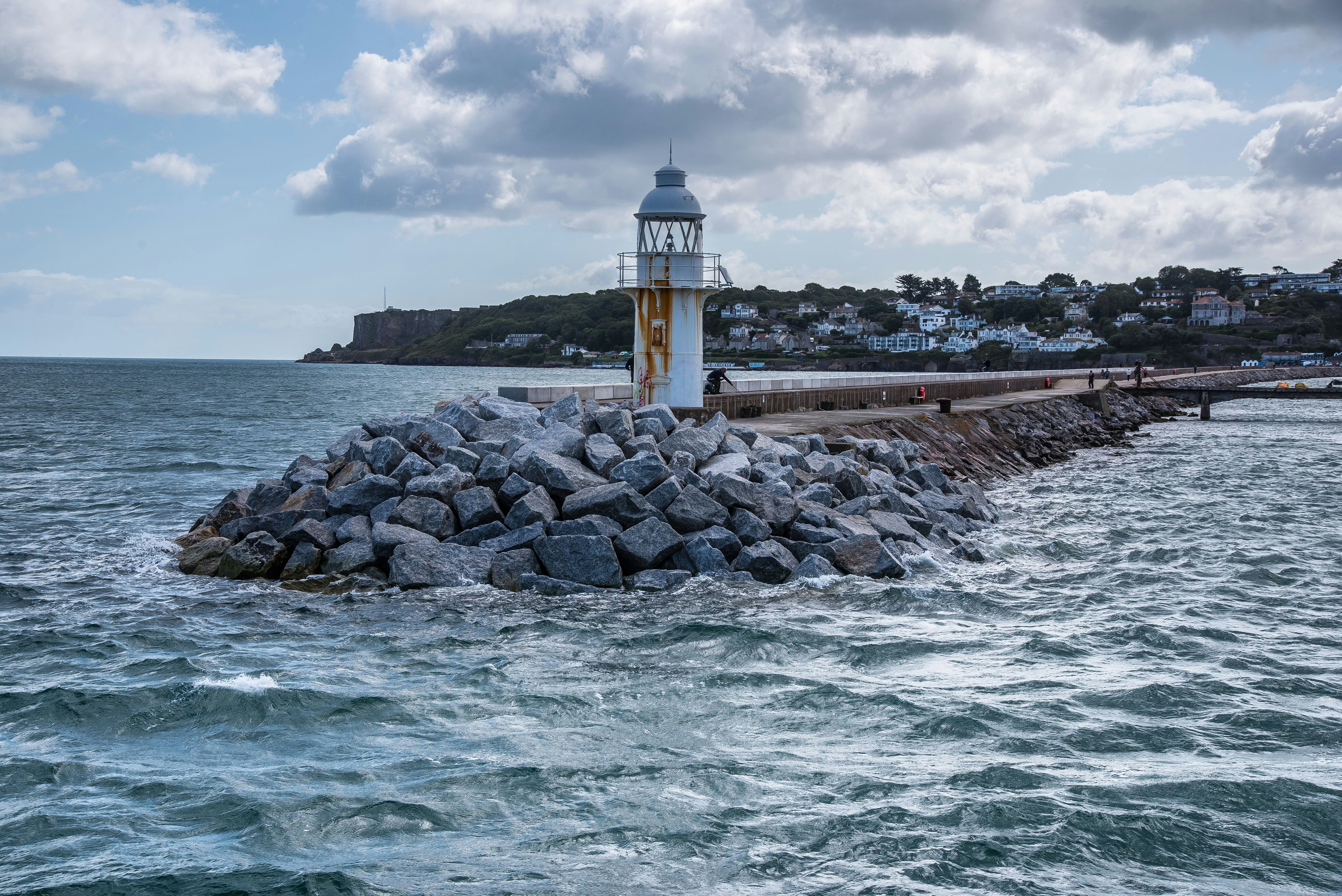 white and brown lighthouse near body of water under white clouds and blue sky during daytime