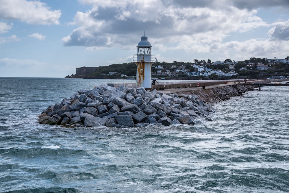 Phare blanc et brun près du plan d’eau sous les nuages blancs et le ciel bleu pendant la journée