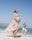 A pregnant woman in a floral dress and flower crown walks along a sandy beach. Another person in casual clothing walks behind her, smiling. The sky is clear and blue, with the ocean in the background.