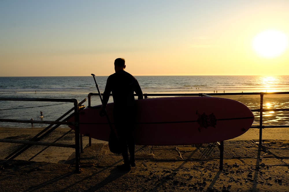 man sitting on brown wooden chair near body of water during sunset