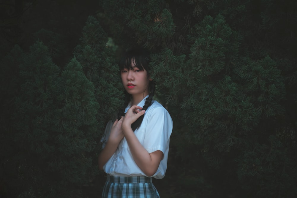 woman in white shirt and blue plaid skirt standing near green plant