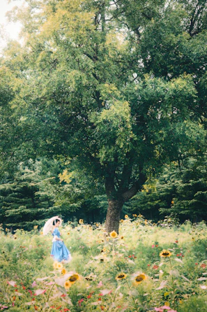 A serene garden scene with a woman in a flowing long dress and delicate veil, hands gently tending to flowers, face turned away.