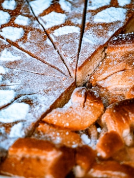 A close-up view of a freshly baked cake with powdered sugar sprinkled on top. The cake is cut into triangular slices, highlighting its moist texture and golden-brown color. The powdered sugar adds a decorative and sweet touch, enhancing its visual appeal.