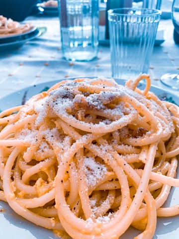 Close-up of a hand sprinkling parmesan cheese over a steaming plate of spaghetti.