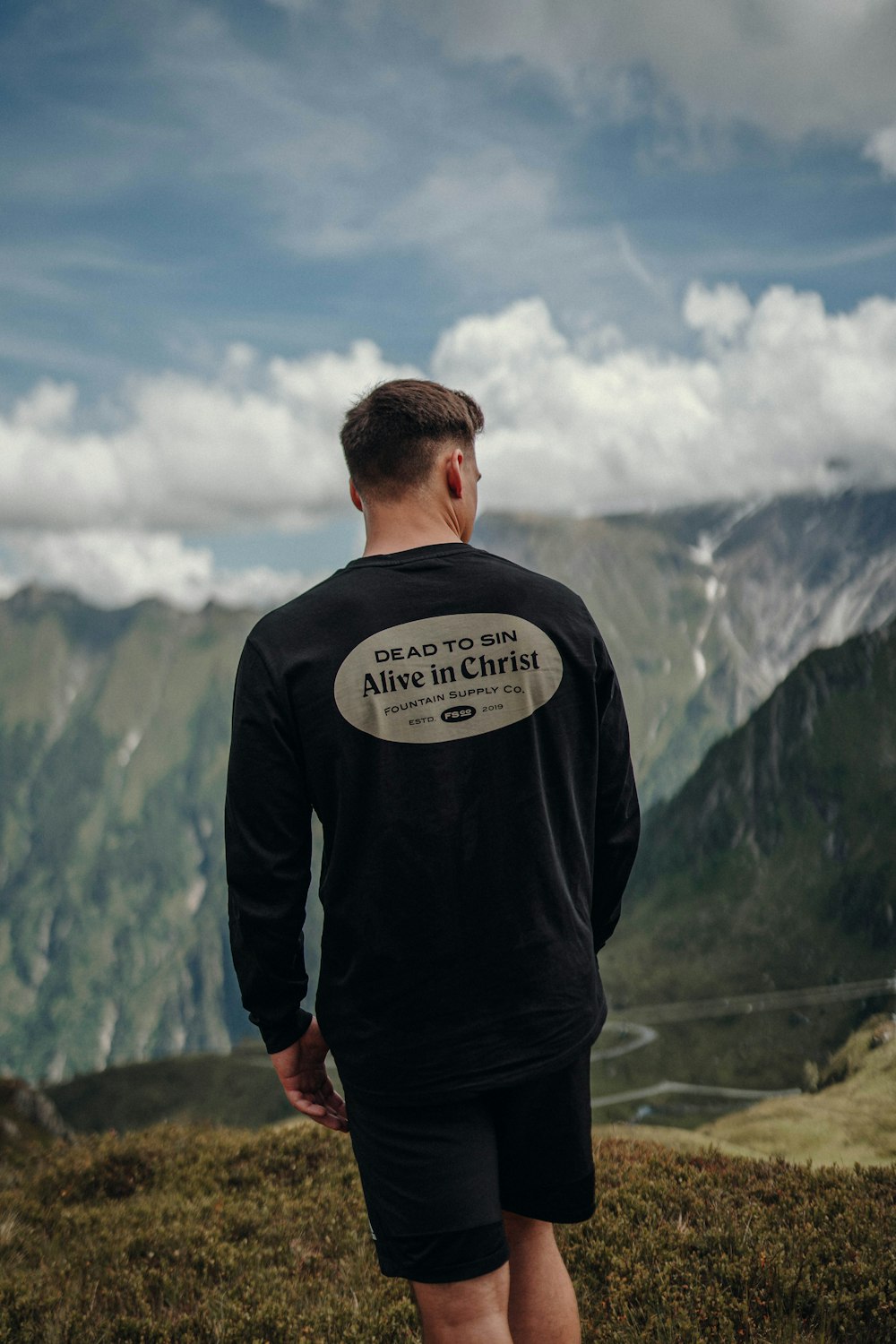 man in black and white long sleeve shirt standing on mountain under blue and white cloudy