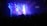 A band is performing on stage in a dimly lit concert venue. Bright stage lights in blue and purple illuminate the musicians. A large crowd is gathered, watching the performance. The stage backdrop features a logo.
