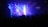 A band is performing on stage in a dimly lit concert venue. Bright stage lights in blue and purple illuminate the musicians. A large crowd is gathered, watching the performance. The stage backdrop features a logo.