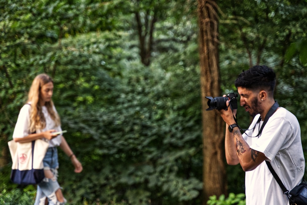 man in white tank top holding black dslr camera