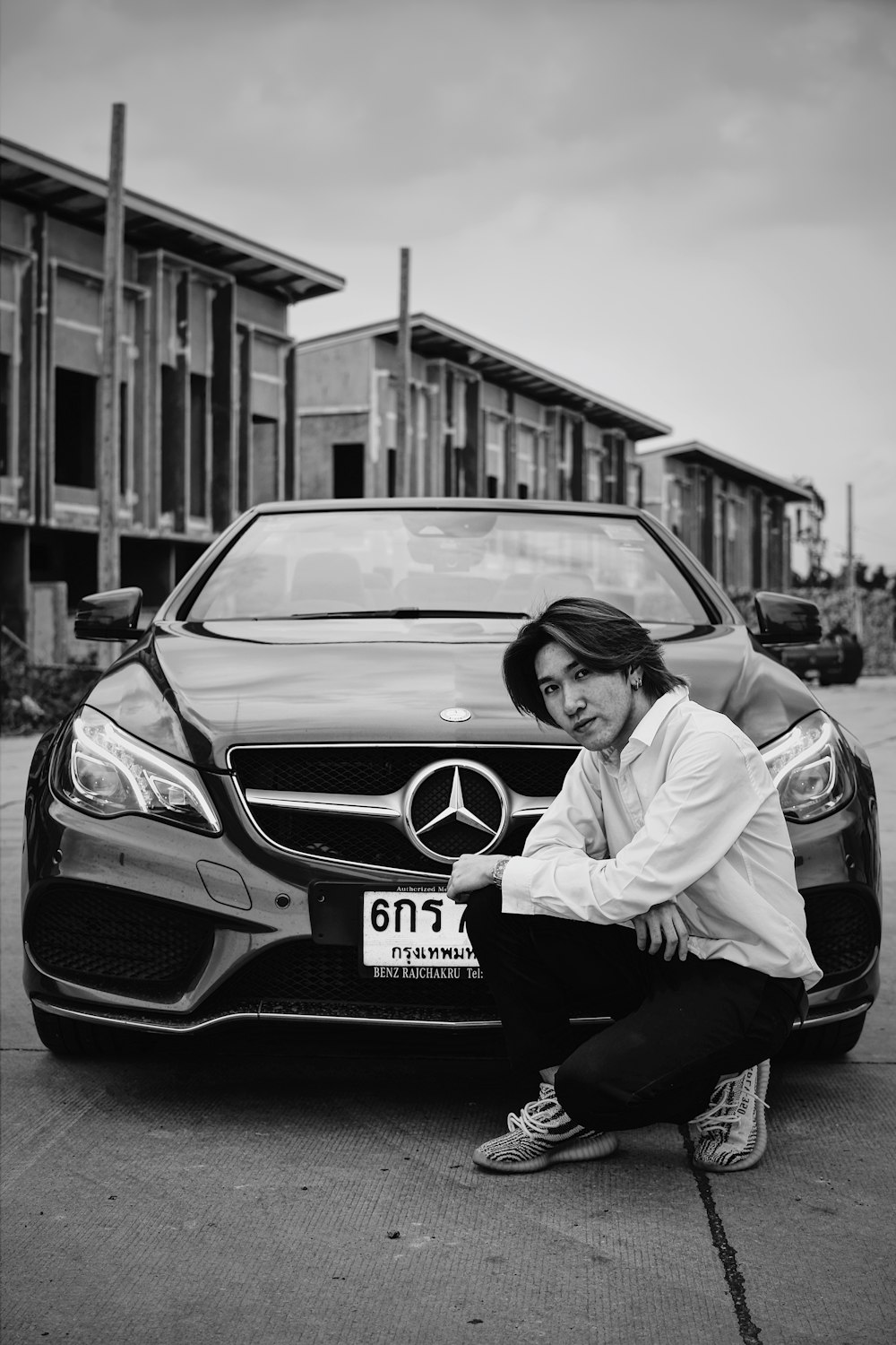 grayscale photo of man in white dress shirt and black pants sitting on mercedes benz car