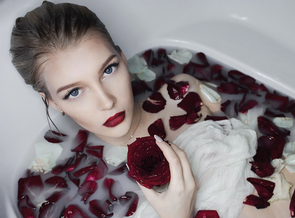 woman in white ceramic bathtub with red petals