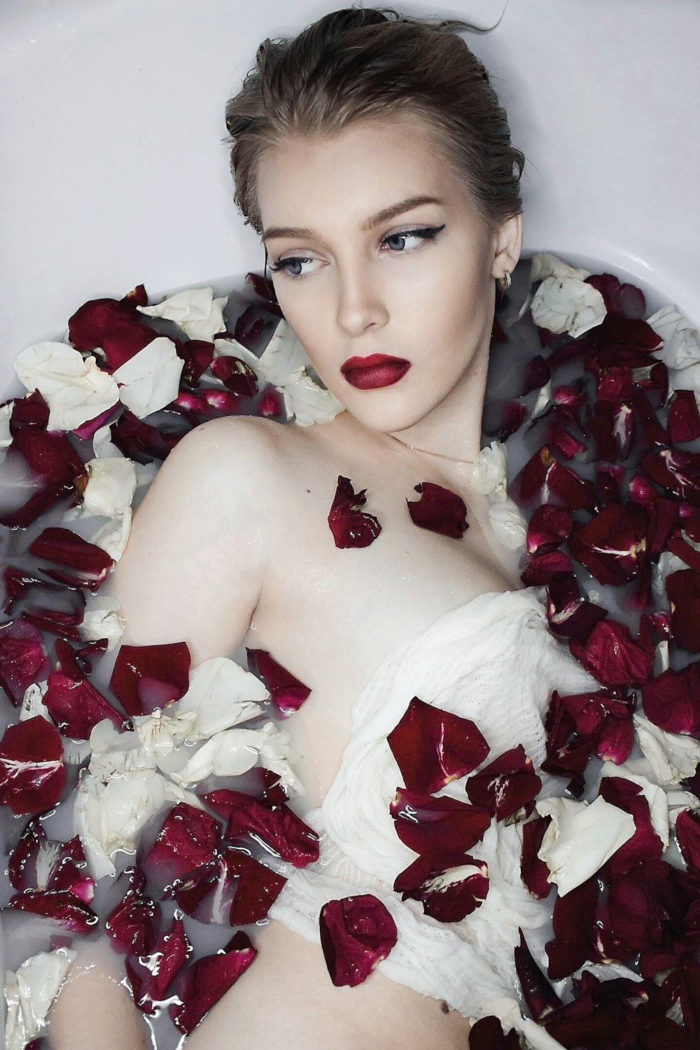 woman in white ceramic bathtub with red petals