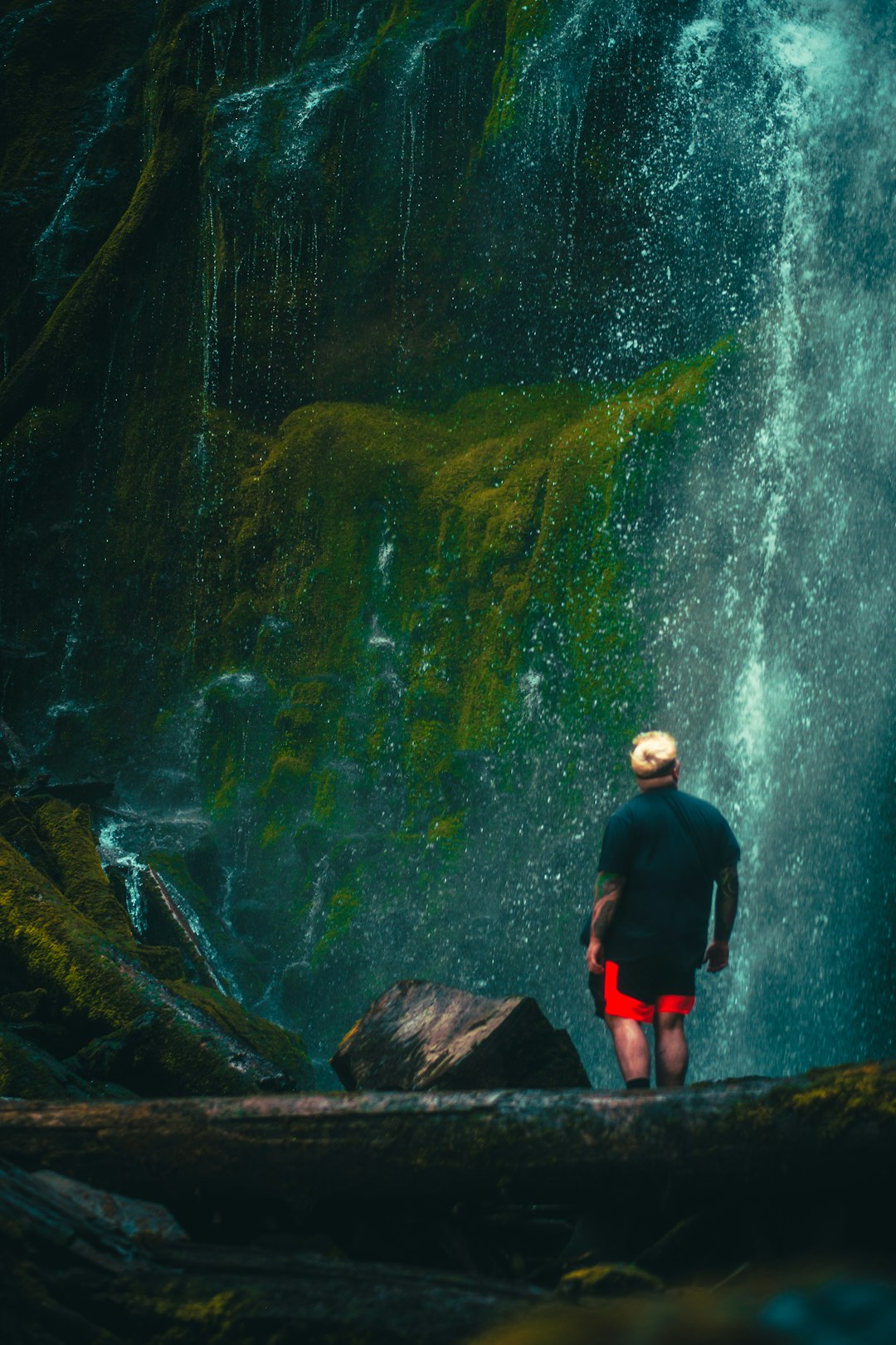 man in black jacket standing on brown rock in front of waterfalls