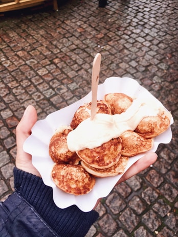 Happy customer enjoying a warm Dutch mini pancake at a cozy outdoor food stall.
