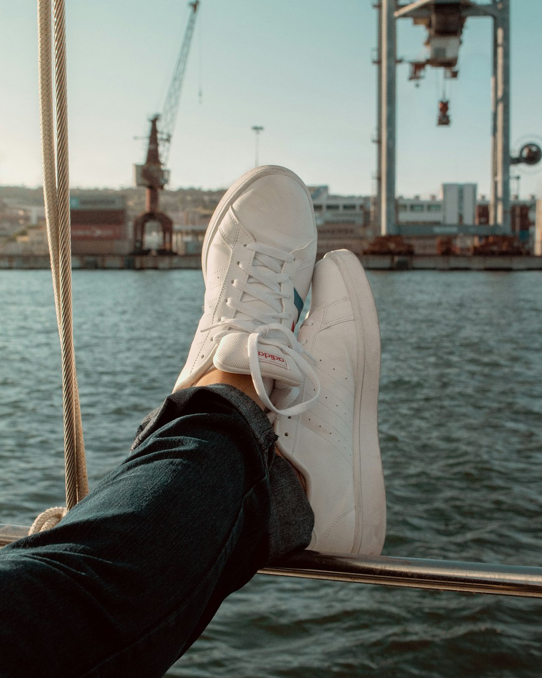 person in blue denim jeans and white nike sneakers sitting on brown wooden dock during daytime