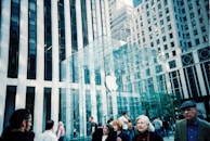 A group of people walking in front of a modern glass building with a recognizable logo. The building is located in an urban setting, surrounded by tall skyscrapers with a combination of reflective glass and stone exteriors.