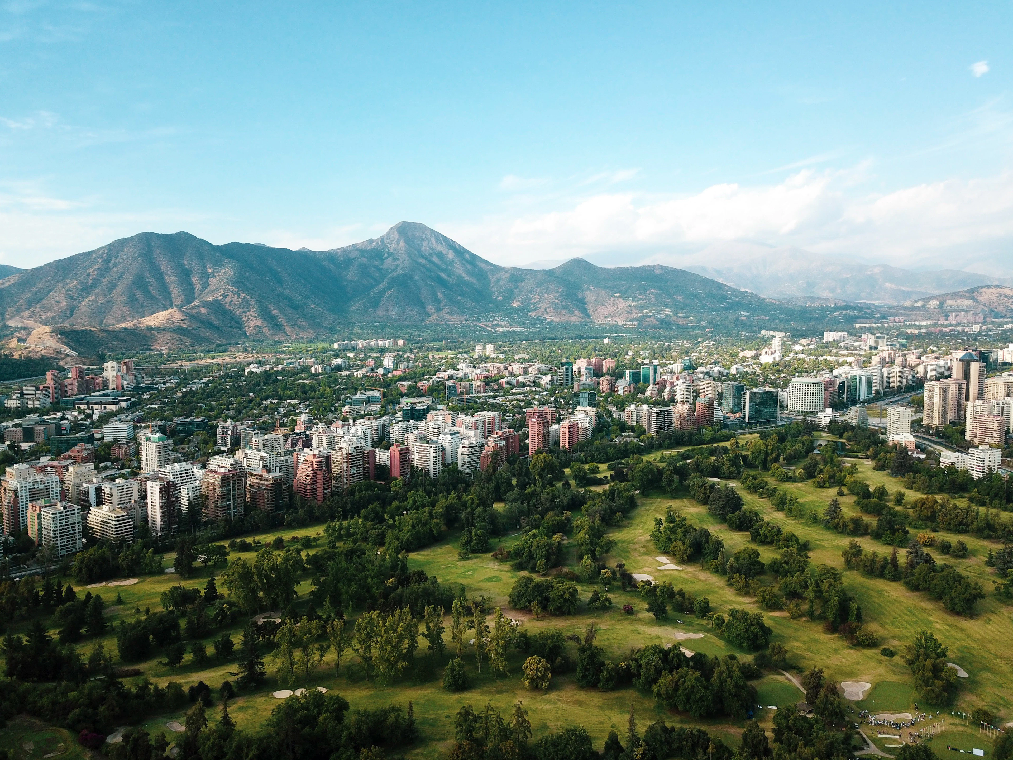 Aerial view over Santiago's leafy eastern districts, residential towers and a green golf course backed by the dry peaks of the Andean foothills