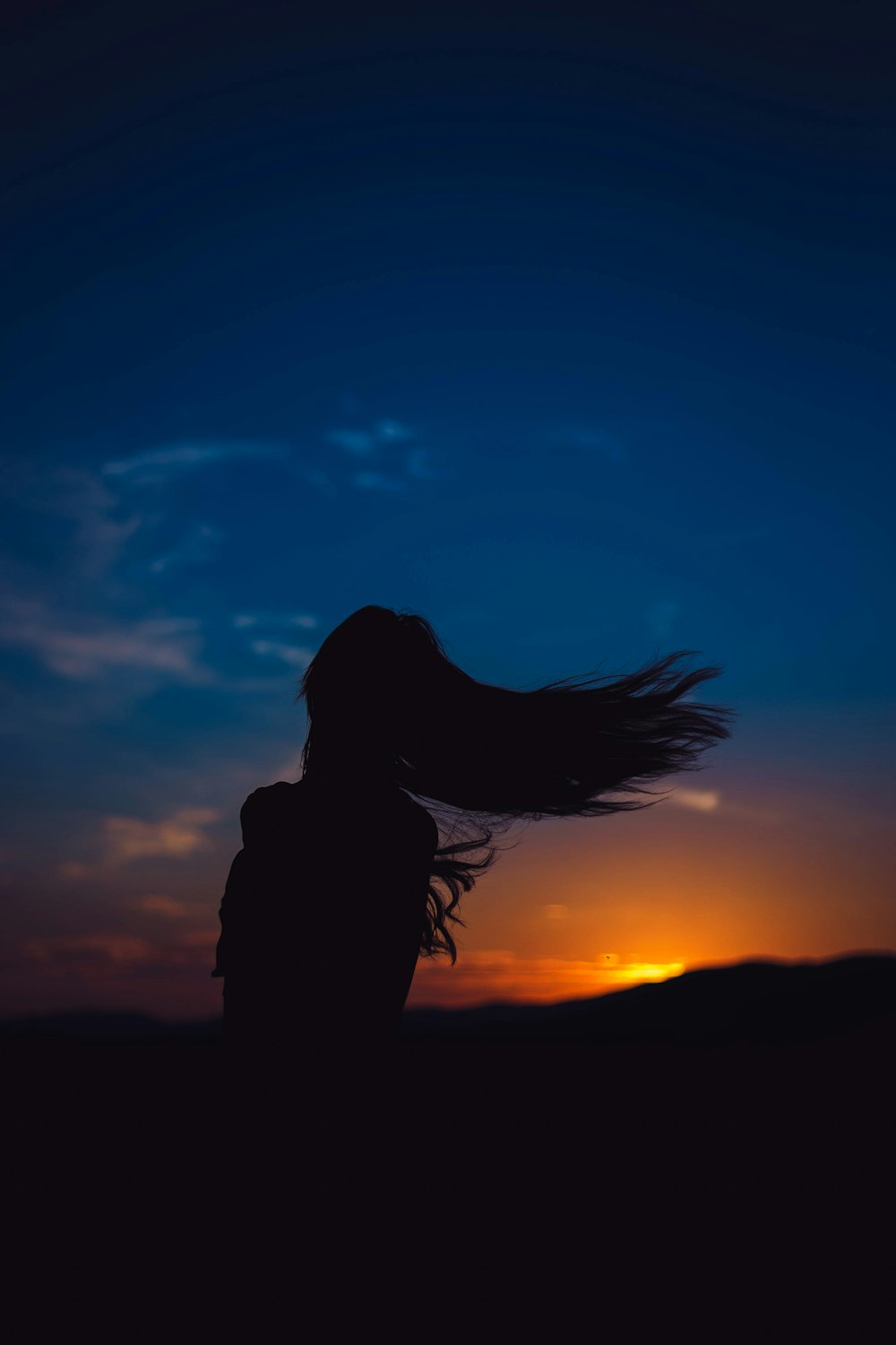 silhouette of woman standing under blue sky during sunset
