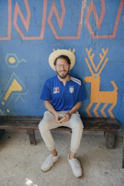 man in blue polo shirt and white pants sitting on brown wooden bench