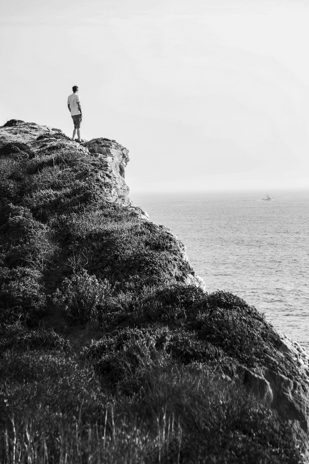 grayscale photo of person standing on rock formation near body of water
