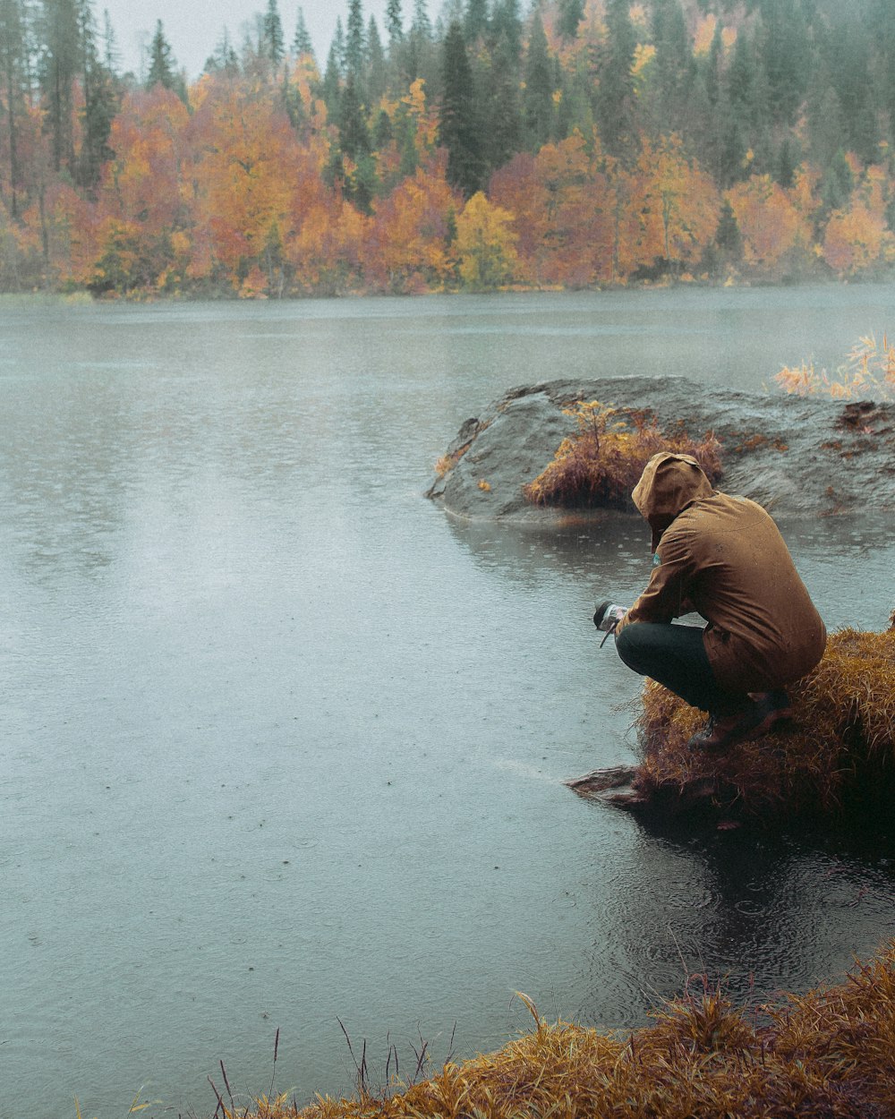 man in brown jacket sitting on rock in river during daytime