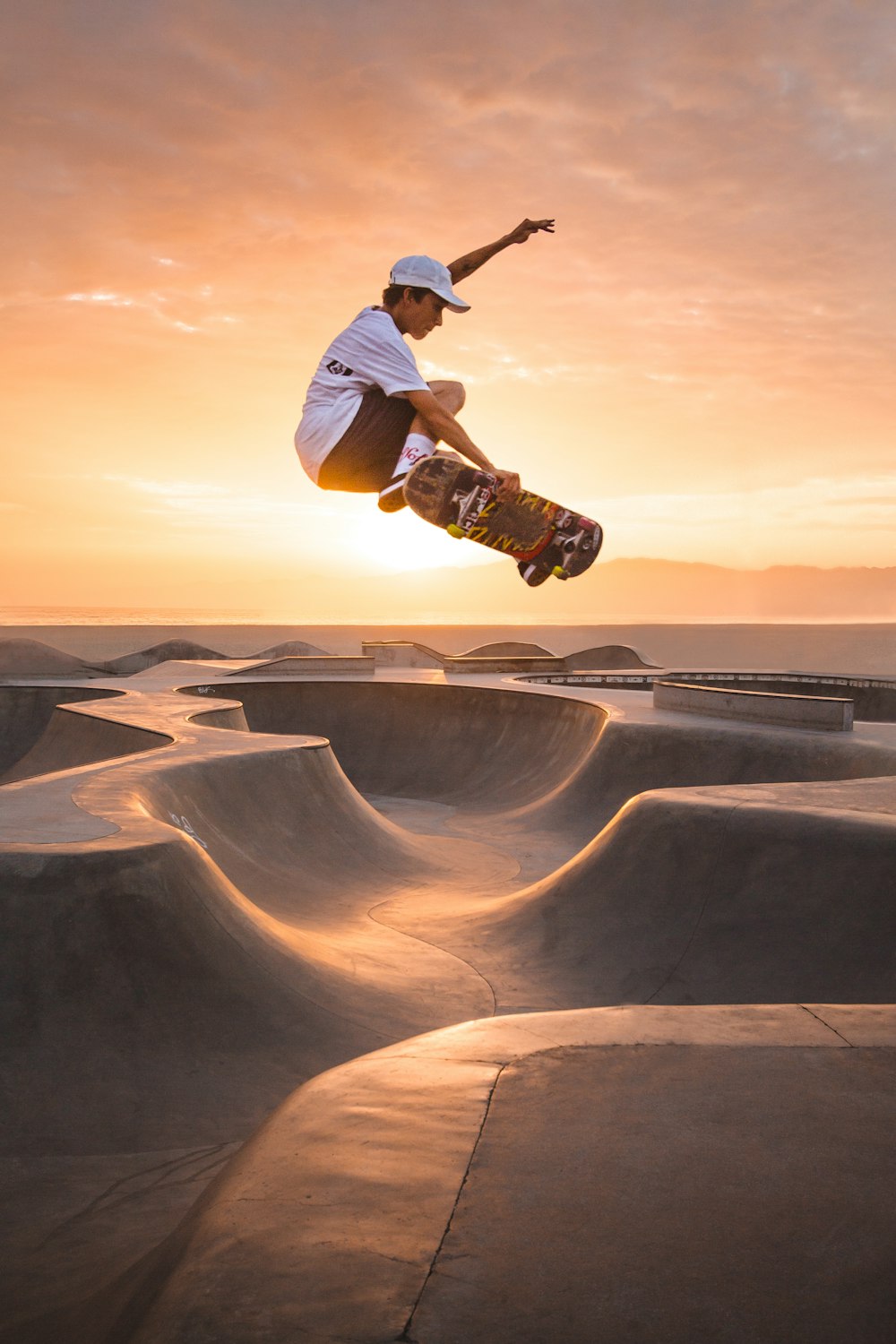 Homem de camiseta branca e calça marrom andando de skate na areia marrom durante o dia