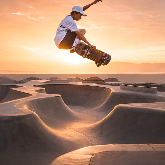 A person jumping on a skateboard in a concrete skatepark at golden hour