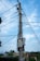 A utility pole with numerous electrical wires and cables attached, set against a partly cloudy sky. The pole is situated near some buildings and trees, contributing to a suburban or rural setting.