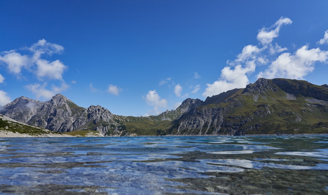 green and brown mountain beside body of water under blue sky during daytime