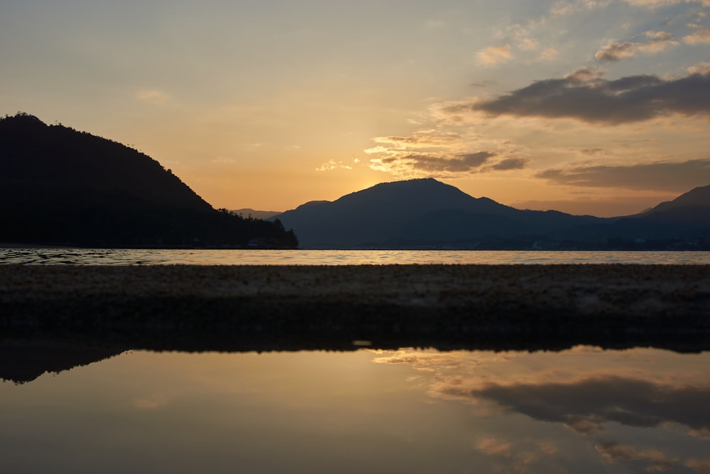 silhouette of mountain near body of water during sunset
