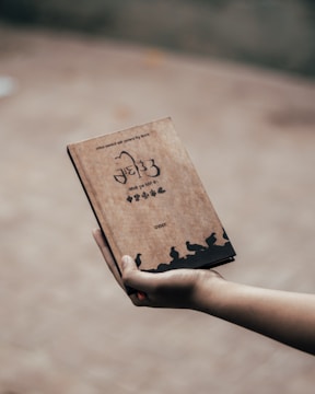 A hand holding a bird identification guidebook next to binoculars.