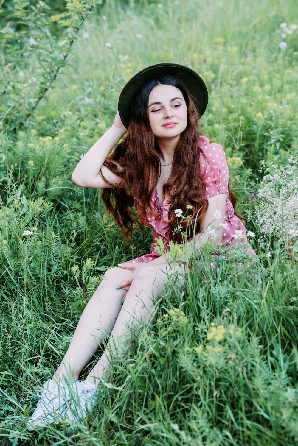 Frau in weißem und rosa Blumenkleid, die tagsüber auf grünem Gras sitzt