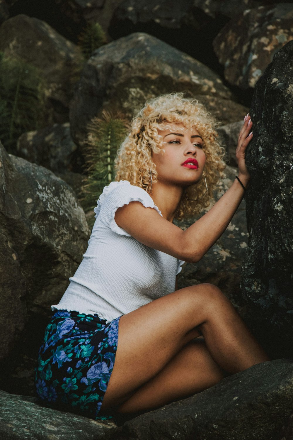 woman in white long sleeve shirt and blue and black floral skirt sitting on rock