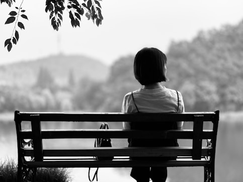 grayscale photo of person sitting on bench