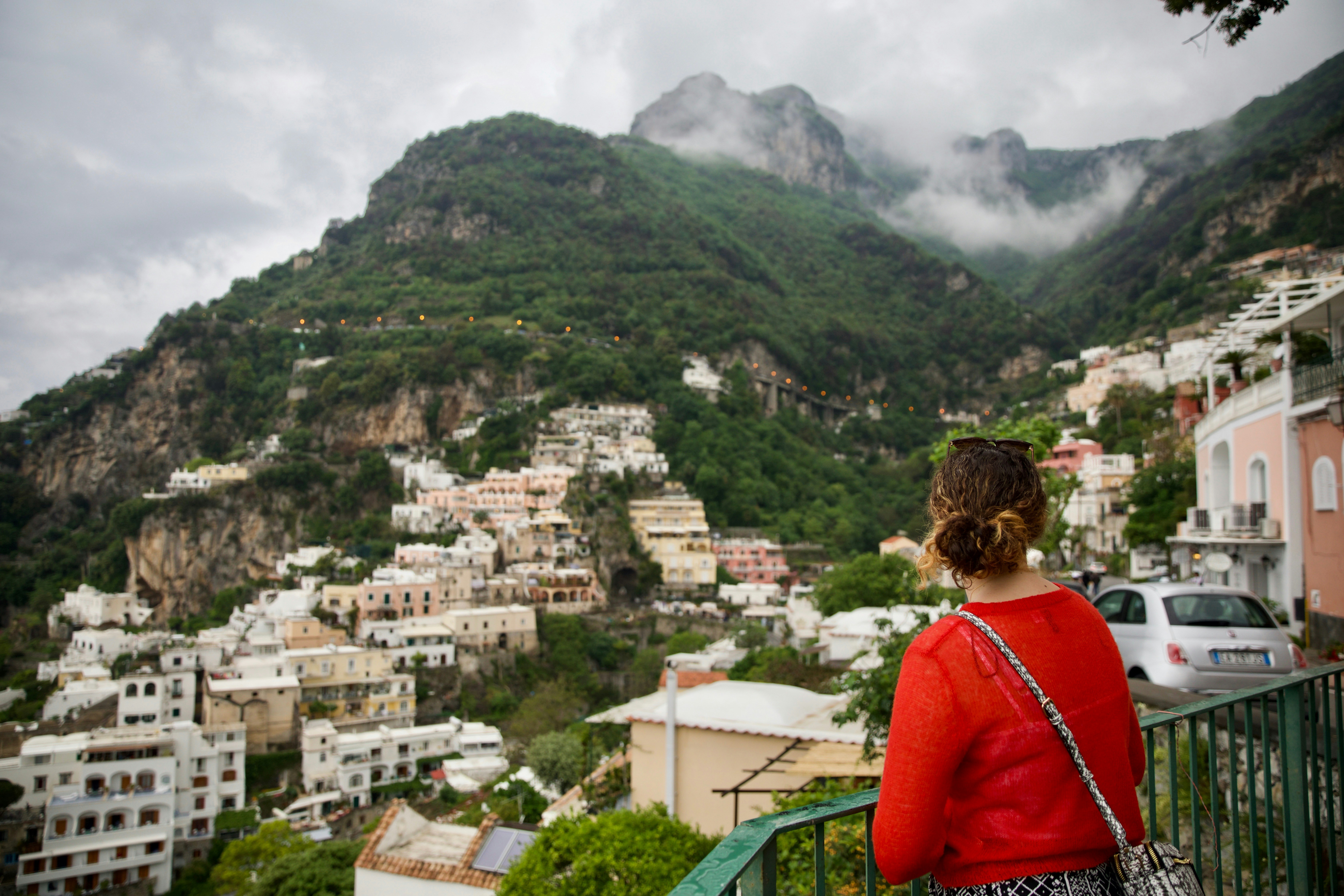 woman in red jacket standing on top of building looking at green mountain during daytime