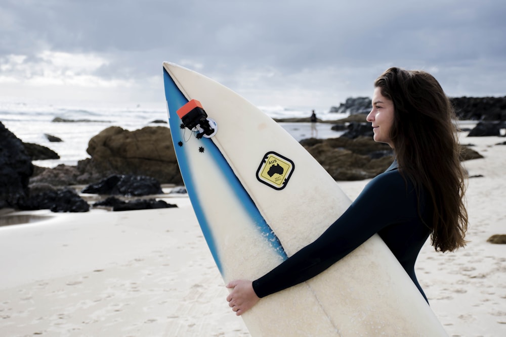 woman in black long sleeve shirt holding white surfboard on beach during daytime
