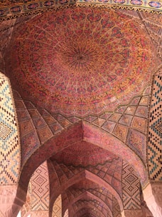 A ceiling adorned with intricate and colorful Persian patterns, featuring floral and geometric motifs. The arches are decorated with similar detailed designs, reflecting traditional Persian architecture.