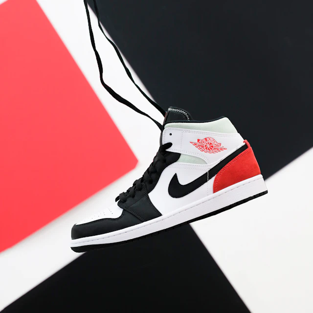 A black, white and red Nike Air Jordan 1 Mid sneaker floating against a plain background