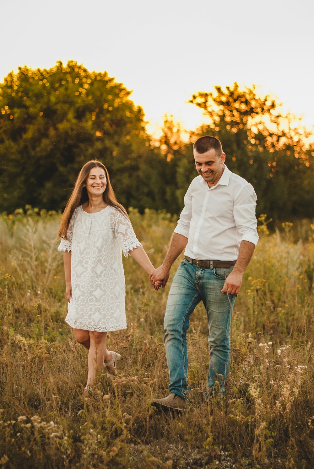 man and woman holding hands while walking on grass field during daytime