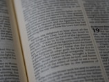 An open book displaying a page filled with text. The text is clearly printed, featuring a mix of normal and bold fonts, with some words emphasized in bold for highlight. The focus is primarily on the left page, while the right page is visible but blurred.
